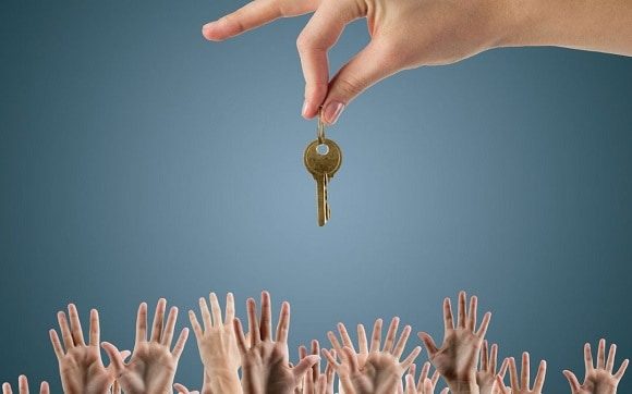 Dozens of hands reaching up to another hand holding house keys