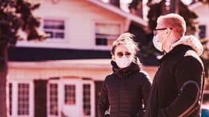 A man and a woman wearing face masks while looking at a house together